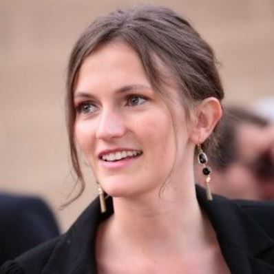 Personne souriant avec des boucles d'oreilles et un blazer foncé.