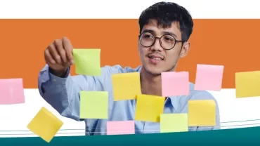 Person arranging colorful sticky notes on a glass board.