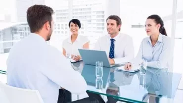 Vier mensen in vergadering aan een glazen tafel met een laptop.