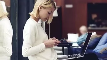 Persoon zit in een lounge met een smartphone en een laptop op schoot.