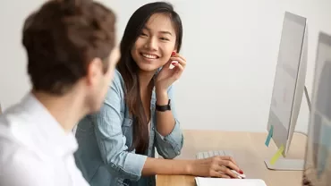Deux personnes discutent à un bureau avec un ordinateur.
