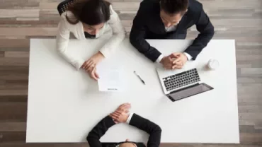 Trois personnes en réunion autour d'une table avec un ordinateur portable.