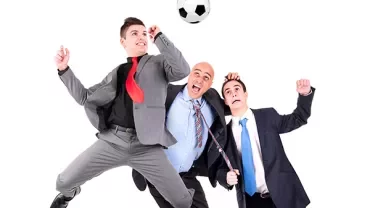 Groupe de personnes en costume sautant pour un ballon de foot.