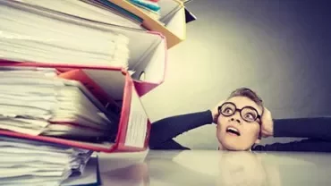 Person overwhelmed by a stack of files and paperwork.