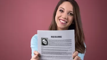 Personne souriant et tenant un CV sur fond rose.
