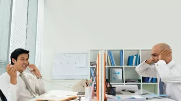 Two people working in an office with one talking on the phone.