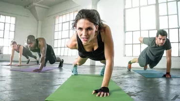 Group doing a plank exercise in a bright fitness room.