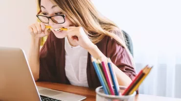 Personne mordant un crayon en regardant un ordinateur portable.