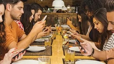 Personnes assises à table, regardant leurs téléphones.