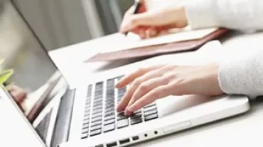 Persoon typend op een laptop en in een notitieboekje schrijvend.