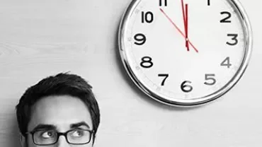 Person wearing glasses looks up at a wall clock showing 10:10.
