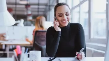Personne parlant au téléphone et écrivant à un bureau dans un bureau lumineux.