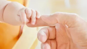 Main de bébé tenant le doigt d'un adulte.