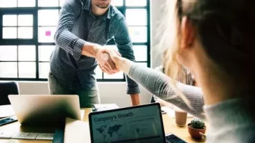 Personnes se serrant la main dans un bureau, un ordinateur portable ouvert sur la table.