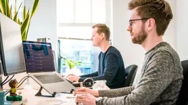 Two people working at computers in an office setting with natural light.