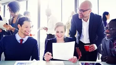 Groupe de personnes dans un bureau lumineux, souriant et examinant des documents.