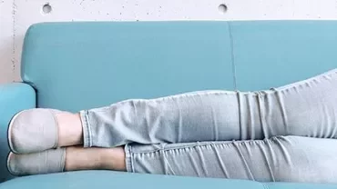Persoon ontspant op een lichtblauwe bank, gekleed in jeans en instapschoenen.