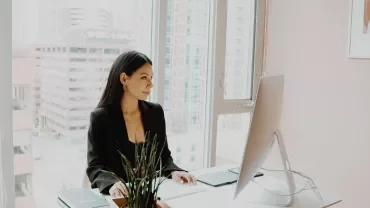 Person at desk working on computer with city view.