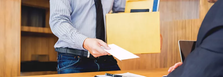Een werknemer, gekleed in overhemd en das, draagt een doos met documenten en overhandigt een ontslagbrief aan zijn baas.