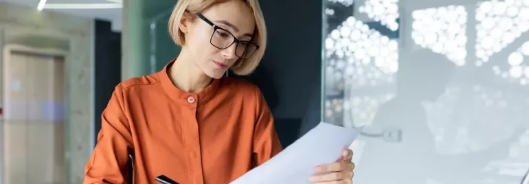 Femme blonde portant des lunettes lisant une feuille de papier
