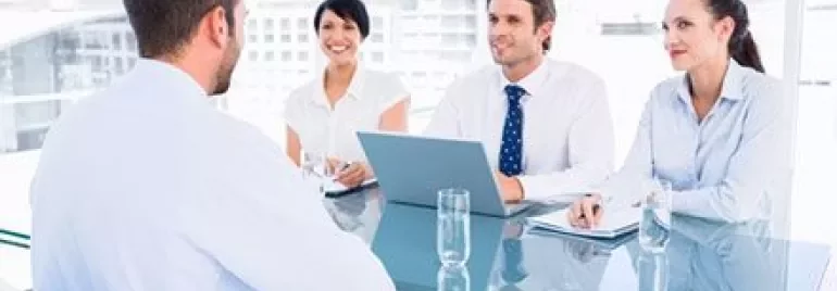 Vier mensen in vergadering aan een glazen tafel met een laptop.