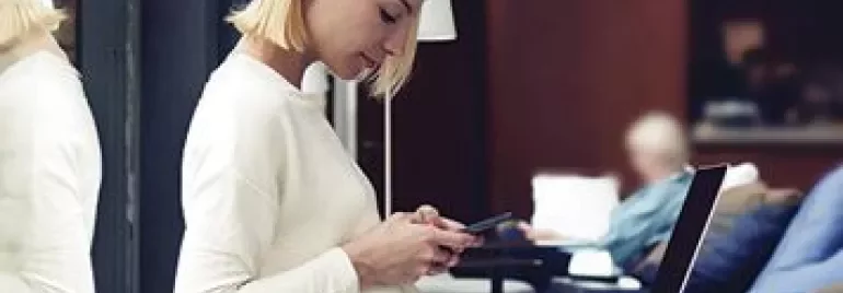 Persoon zit in een lounge met een smartphone en een laptop op schoot.