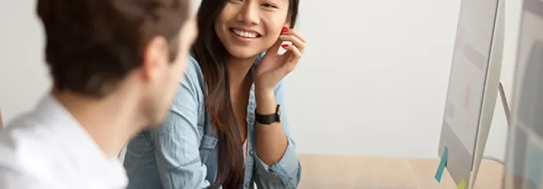 Two people engaged in a conversation at a desk with a computer.