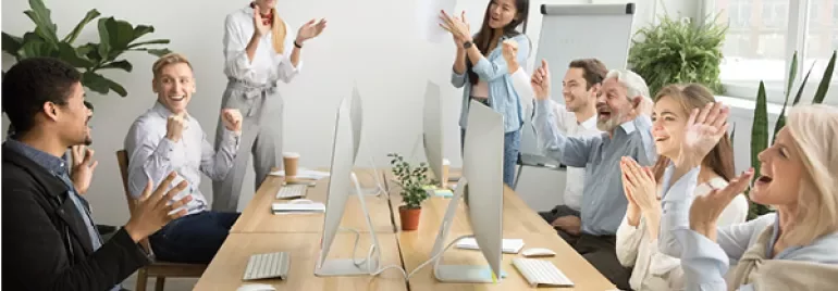 Mensen applaudisseren en lachen in een vergaderruimte rond een tafel.