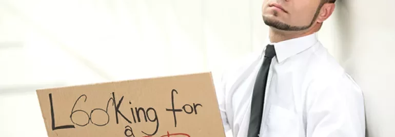 Person holding a cardboard sign reading 'Looking for a Job' while sitting against a wall.