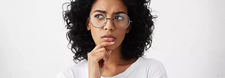 Personne aux cheveux bouclés portant des lunettes, d'apparence pensive.