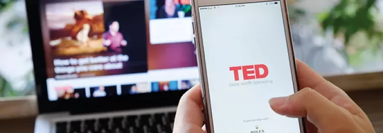 Person using TED app on smartphone with laptop in background.