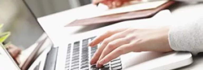 Personne tapant sur un ordinateur portable et écrivant dans un carnet.