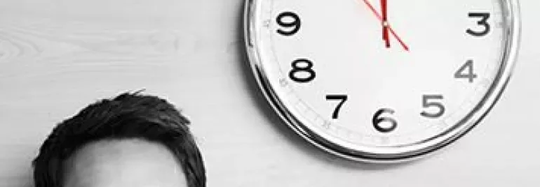 Personne avec des lunettes regarde une horloge murale indiquant 10h10.