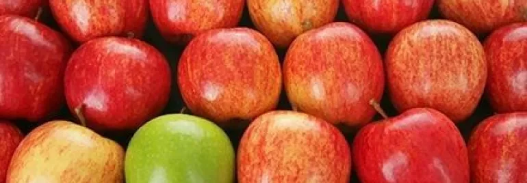 Een groep rode appels met een groene appel ertussen.