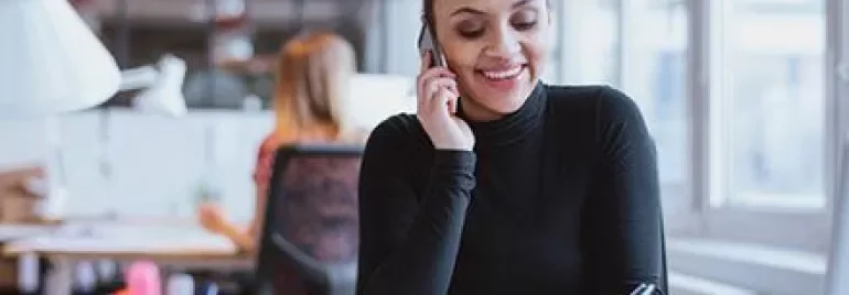 Personne parlant au téléphone et écrivant à un bureau dans un bureau lumineux.