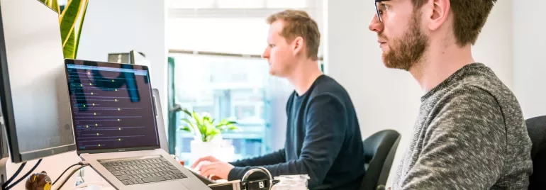 Two people working at computers in an office setting with natural light.