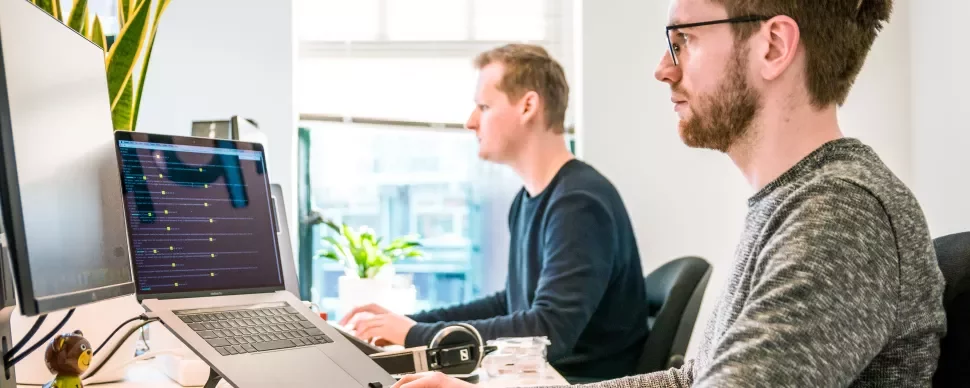 Twee mensen die in een goed verlichte kantooromgeving op computers werken.
