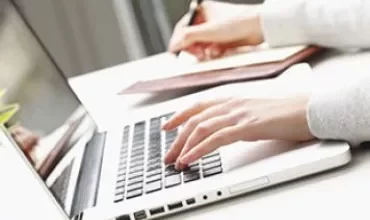 Persoon die typt op een laptop en schrijft in een notitieboekje.